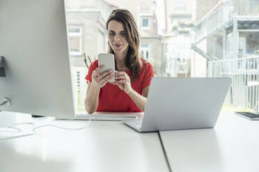 Female professional using mobile phone while sitting at desk - UUF24404