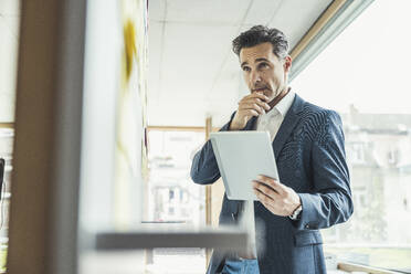 Businessman with digital tablet looking at whiteboard - UUF24416