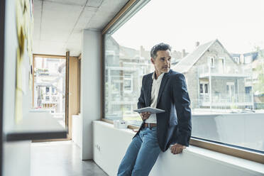 Thoughtful businessman looking through window while standing at office - UUF24418