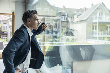 Businessman looking through window while standing in office - UUF24420