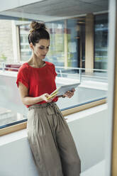 Weibliche Fachkraft, die ein digitales Tablet benutzt und sich an ein Fenster lehnt - UUF24429