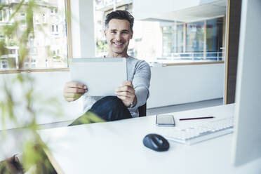 Businessman with digital tablet sitting by desk - UUF24445
