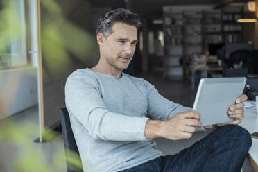 Männlicher Geschäftsmann, der ein digitales Tablet bei der Arbeit im Büro benutzt - UUF24447