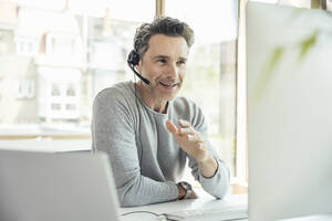 Businessman with headset discussing through video call on computer in office - UUF24451