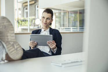 Geschäftsfrau mit digitalem Tablet am Schreibtisch sitzend - UUF24460