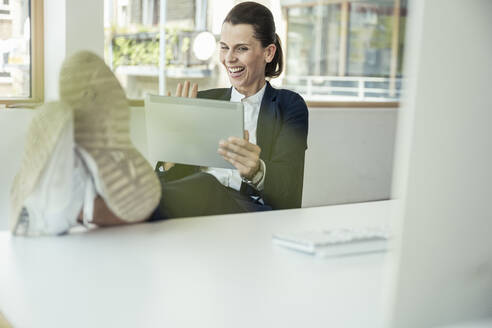 Fröhliche Geschäftsfrau winkt mit der Hand zu einem Videoanruf über ein digitales Tablet im Büro - UUF24463