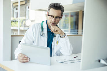 Male doctor using digital tablet while sitting at office - UUF24466