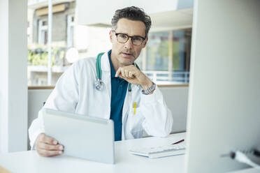 Male general practitioner with digital tablet at office - UUF24467