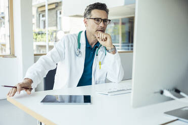 Male doctor with hand on chin using computer at office - UUF24470