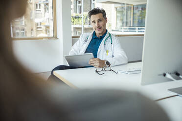 Männliche Fachkraft mit digitalem Tablet, die einen Patienten am Schreibtisch im Büro aufklärt - UUF24473