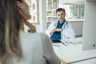 Männlicher Arzt im Gespräch mit einer Patientin im Büro - UUF24474