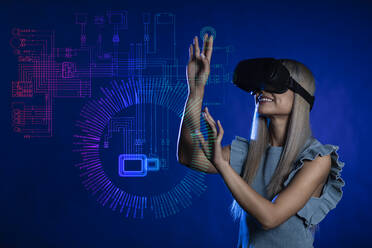 Lächelnde junge Frau mit Virtual-Reality-Simulator gestikuliert über blauem Hintergrund - EIF01925