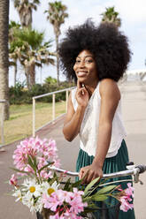 Afro-Frau lächelt, während sie mit dem Fahrrad auf der Straße steht - VEGF04797