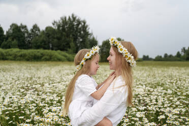 Smiling mother carrying daughter at chamomile field - EYAF01707