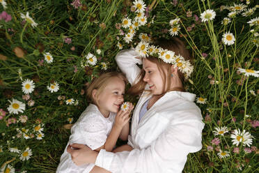 Smiling blond woman resting with daughter amidst chamomile plants - EYAF01710