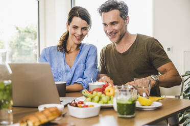 Mann und Frau beobachten Laptop beim Frühstück zu Hause - UUF24487