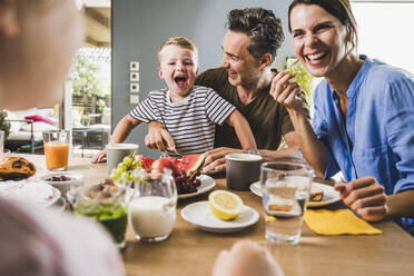 Smiling woman looking at daughter while having breakfast at home - UUF24497