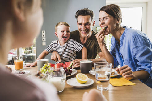 Father and mother looking at daughter while having breakfast at home - UUF24498