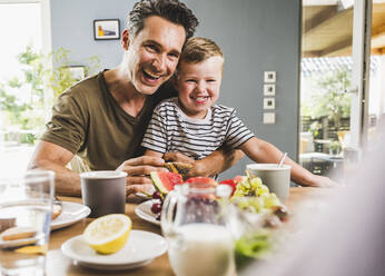 Happy father and son having breakfast at home - UUF24499