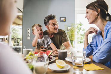 Playful father and son teasing woman while having breakfast at home - UUF24500