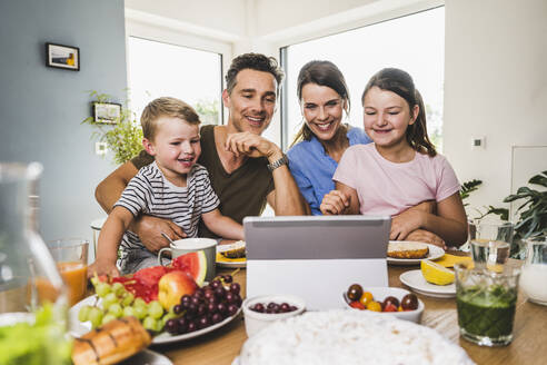 Familie betrachtet digitales Tablet auf dem Tisch, während sie zu Hause frühstücken - UUF24501