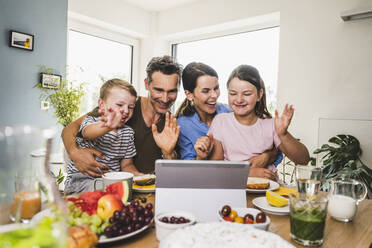 Happy family waving during video call on digital tablet at home - UUF24502