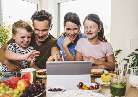 Lächelnde Familie gestikuliert während eines Videoanrufs auf dem Laptop zu Hause - UUF24504