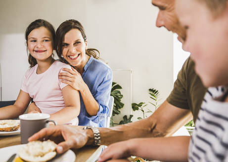 Lächelnde Tochter und Mutter betrachten den Vater beim Frühstück - UUF24506