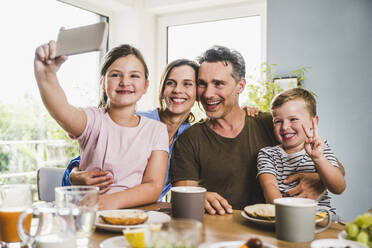 Lächelndes Mädchen nimmt Selfie mit Familie zu Hause - UUF24508