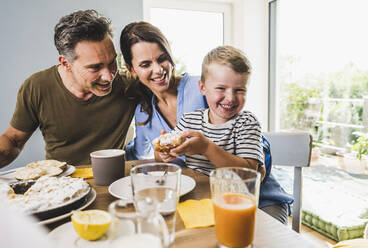 Lächelnder Junge hält Kuchen beim Frühstück mit der Familie zu Hause - UUF24514