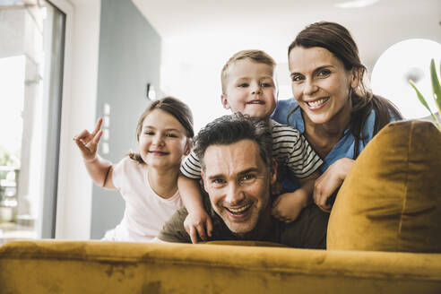 Girl making peace sign while playing with family on sofa at home - UUF24518