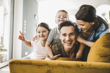 Woman looking at man while playing with son and daughter on sofa at home - UUF24519