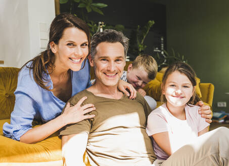 Mann, der mit seiner Familie zu Hause auf dem Sofa sitzt, an einem sonnigen Tag - UUF24521