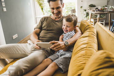 Man sitting with son on sofa while using smart phone at home - UUF24527