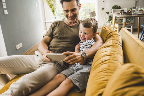 Mann sitzt mit seinem Sohn auf dem Sofa und benutzt zu Hause sein Smartphone - UUF24527