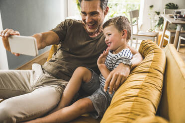 Father taking selfie with son through mobile phone at home - UUF24528