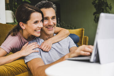 Woman embracing man using digital tablet at home - UUF24535