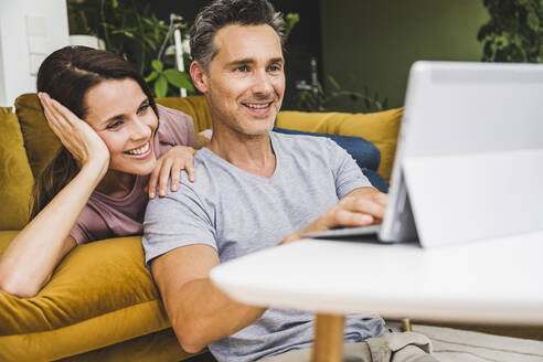 Woman lying on sofa while man using digital tablet at home - UUF24536