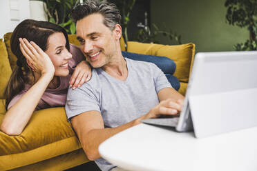 Man and woman looking at each other while using digital tablet at home - UUF24537