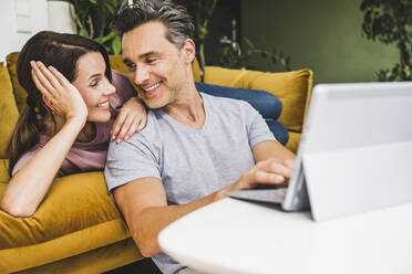 Mann und Frau schauen sich an, während sie ein digitales Tablet zu Hause benutzen - UUF24537