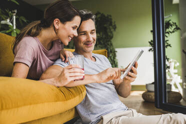 Frau hält ein Saftglas, während ein Mann ein digitales Tablet zu Hause benutzt - UUF24541