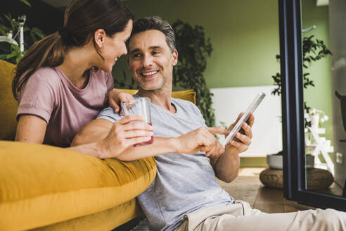 Mann schaut Frau an, während er ein digitales Tablet zu Hause hält - UUF24542