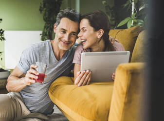 Woman with digital tablet looking at man holding juice glass at home - UUF24547