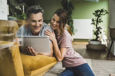 Frau mit Arm um Mann mit digitalem Tablet auf Sofa zu Hause - UUF24550