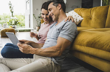 Woman holding water glass while man using digital tablet at home - UUF24552