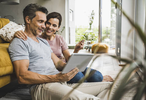 Frau hält Kreditkarte, während sie mit einem Mann zusammensitzt, der ein digitales Tablet zu Hause benutzt - UUF24553