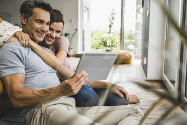 Woman embracing man holding digital tablet at home - UUF24555