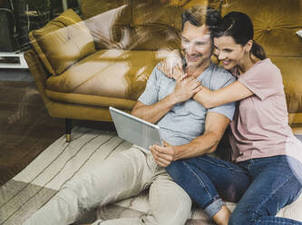 Man and woman using digital tablet at home seen through glass - UUF24556