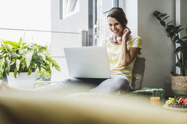 Smiling woman using laptop at home - UUF24558