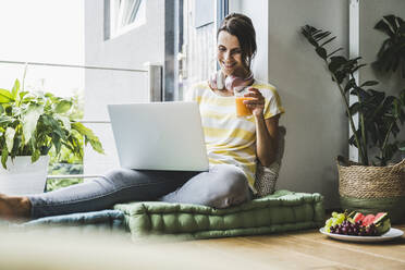 Woman holding juice while using laptop at home - UUF24560